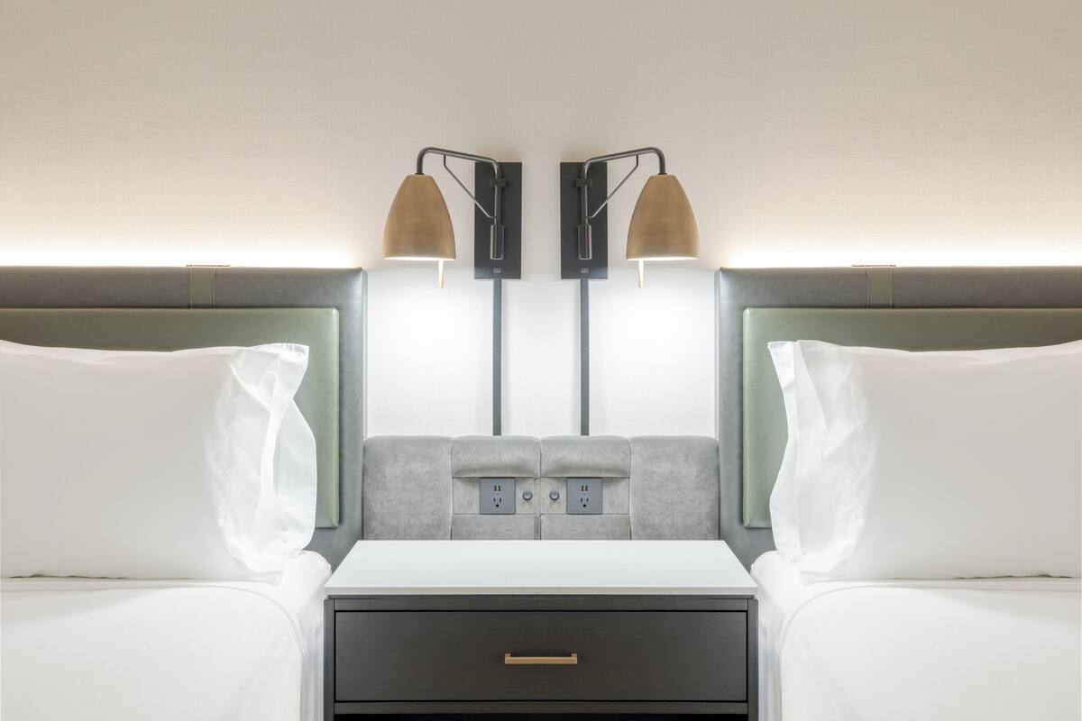 Una habitación de hotel con dos camas, una mesita de noche y una lámpara de pared.
