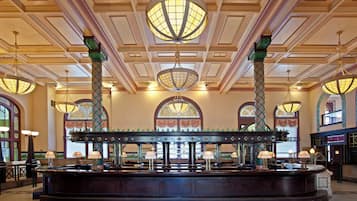 A grand lobby with a central bar, ornate columns, and large chandeliers.