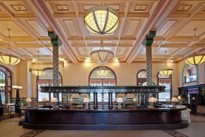 A grand lobby with a central bar, ornate columns, and large chandeliers.
