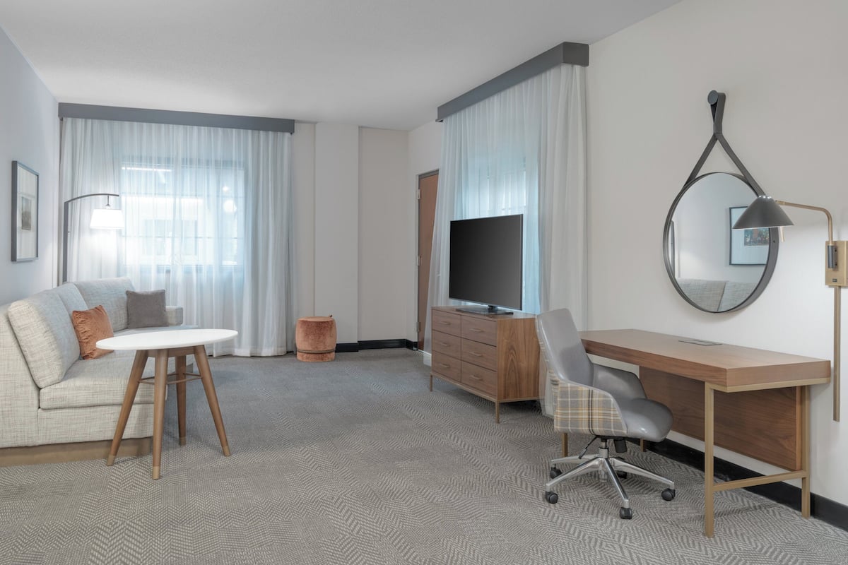 Una habitación de hotel con sofá, escritorio, televisor y lámpara.