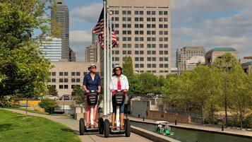 Dos personas realizan un recorrido en Segway en un entorno urbano, con edificios y un canal al fondo.