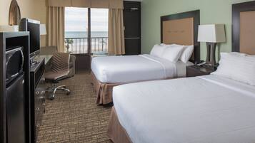 A hotel room with two beds, a desk, a chair, a television, and a view of the beach.