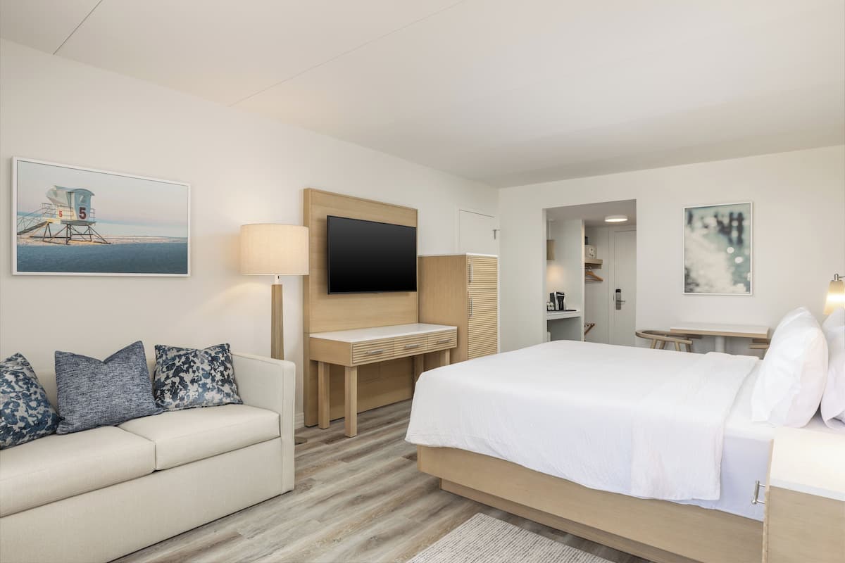 Ein Hotelzimmer mit einem Bett, einem Schreibtisch, einem Fernseher, einer Couch und Kunstwerken an den Wänden.