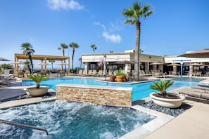 A pool area with lounge chairs, palm trees, and a hot tub.