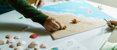 Una persona trabajando en un proyecto artístico con temática de playa, utilizando conchas marinas y un mapa.