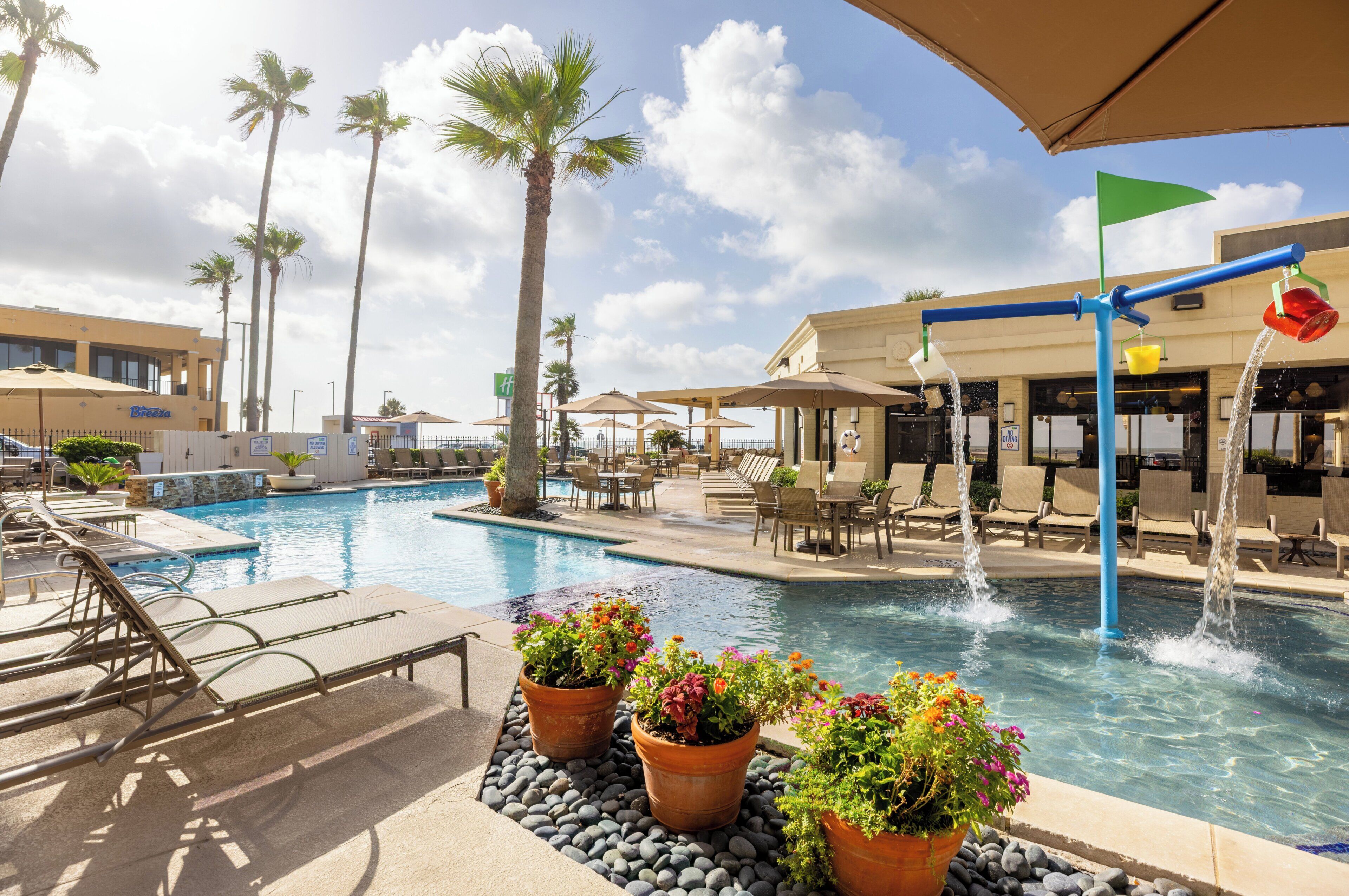 A hotel pool area with lounge chairs, a water feature, and potted plants.