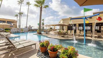 A hotel pool area with lounge chairs, a water feature, and potted plants.