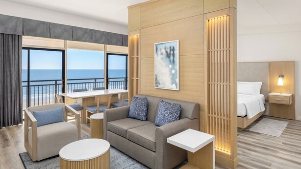 Quarto de hotel moderno com varanda, sofá, mesa de jantar e uma cama.