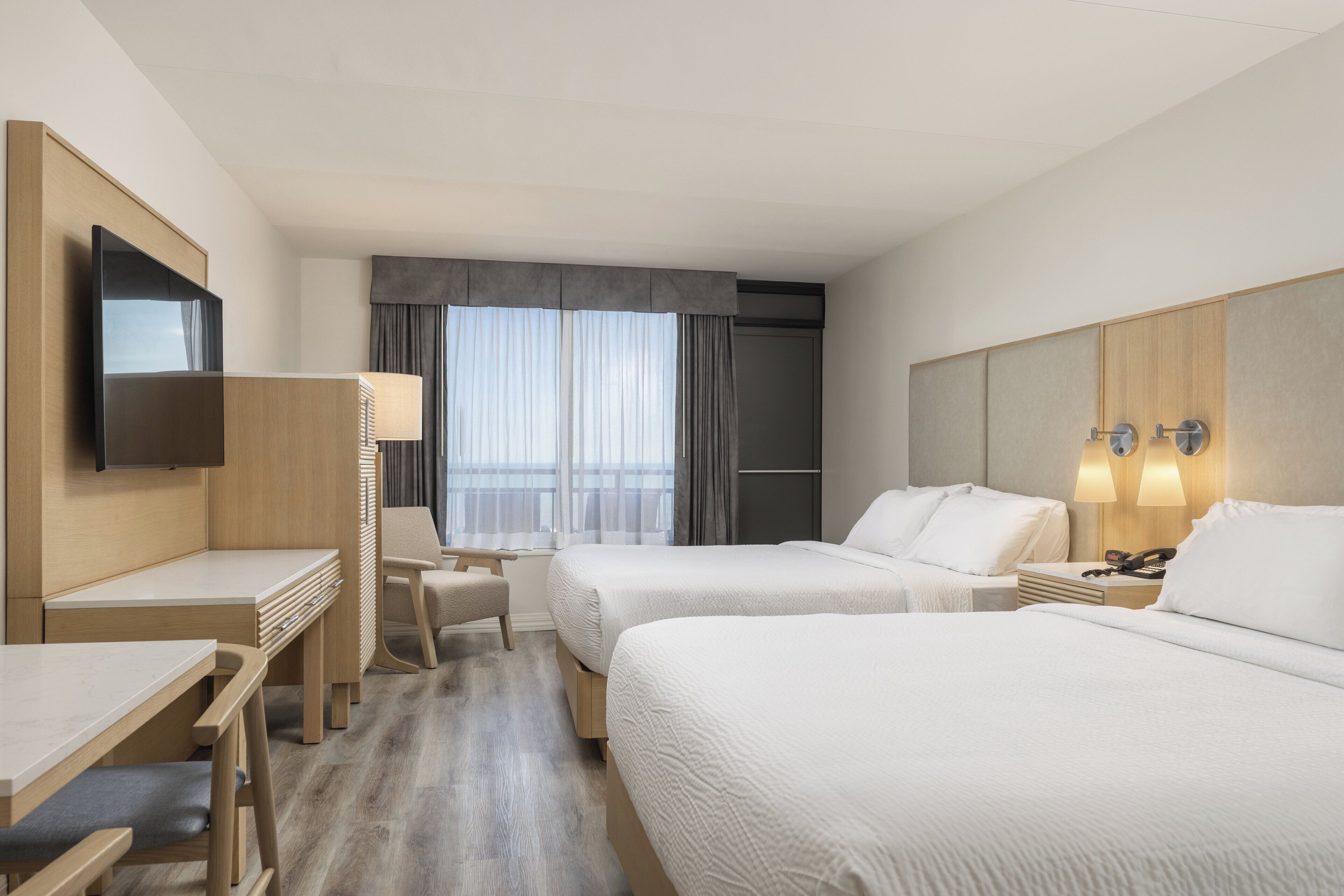 Habitación de hotel con dos camas, un escritorio, una silla, un televisor y una ventana con cortinas.