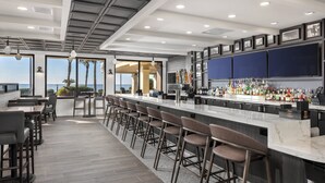 Uma área de bar moderna com um balcão longo, banquetas e vista para o oceano.