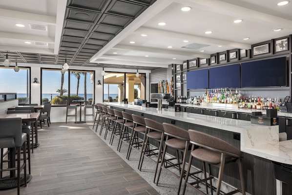 Een moderne bar met een lange toonbank, barstoelen en uitzicht op de oceaan.