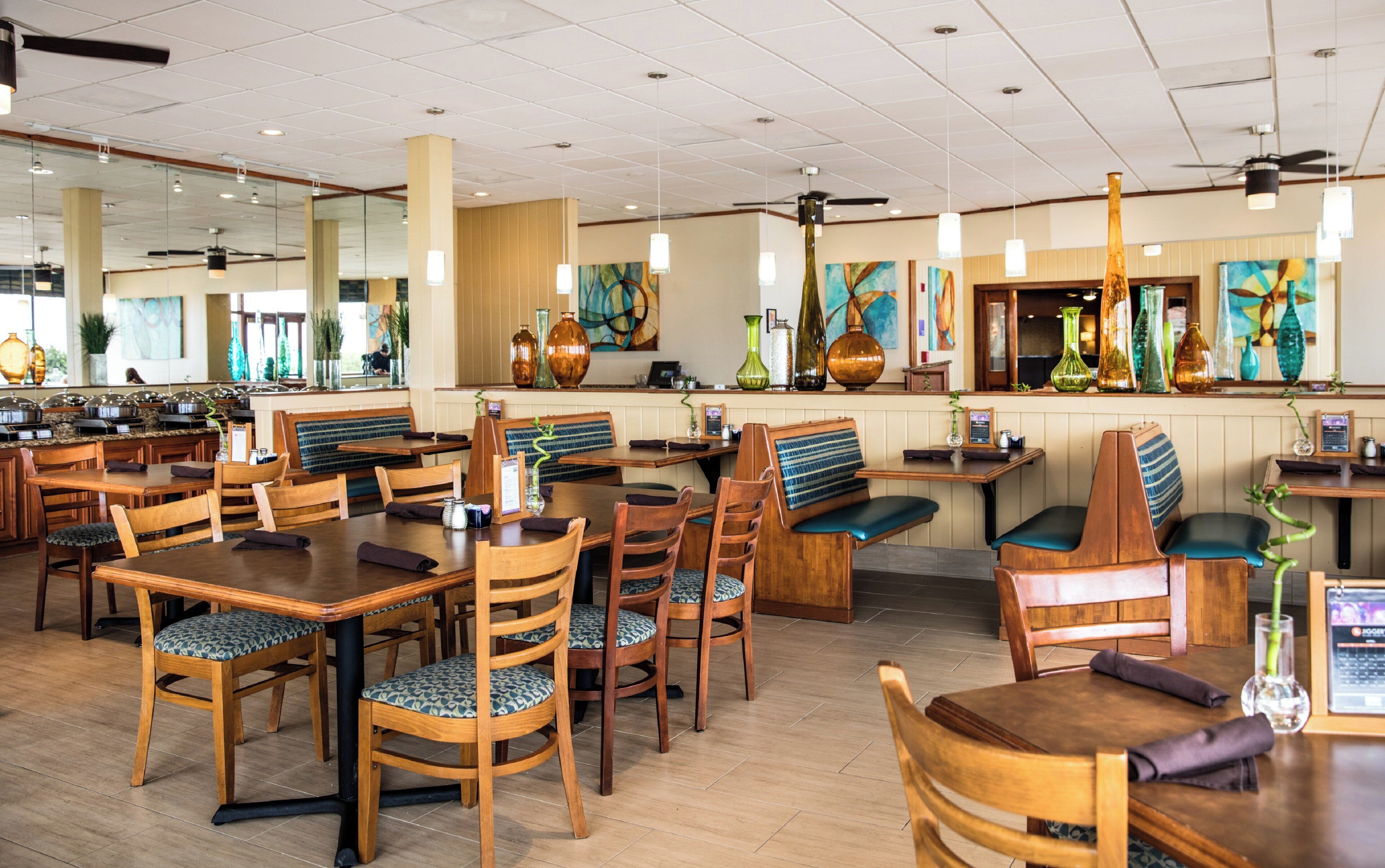 A restaurant with wooden tables and chairs, a buffet area, and decorative vases on the walls.