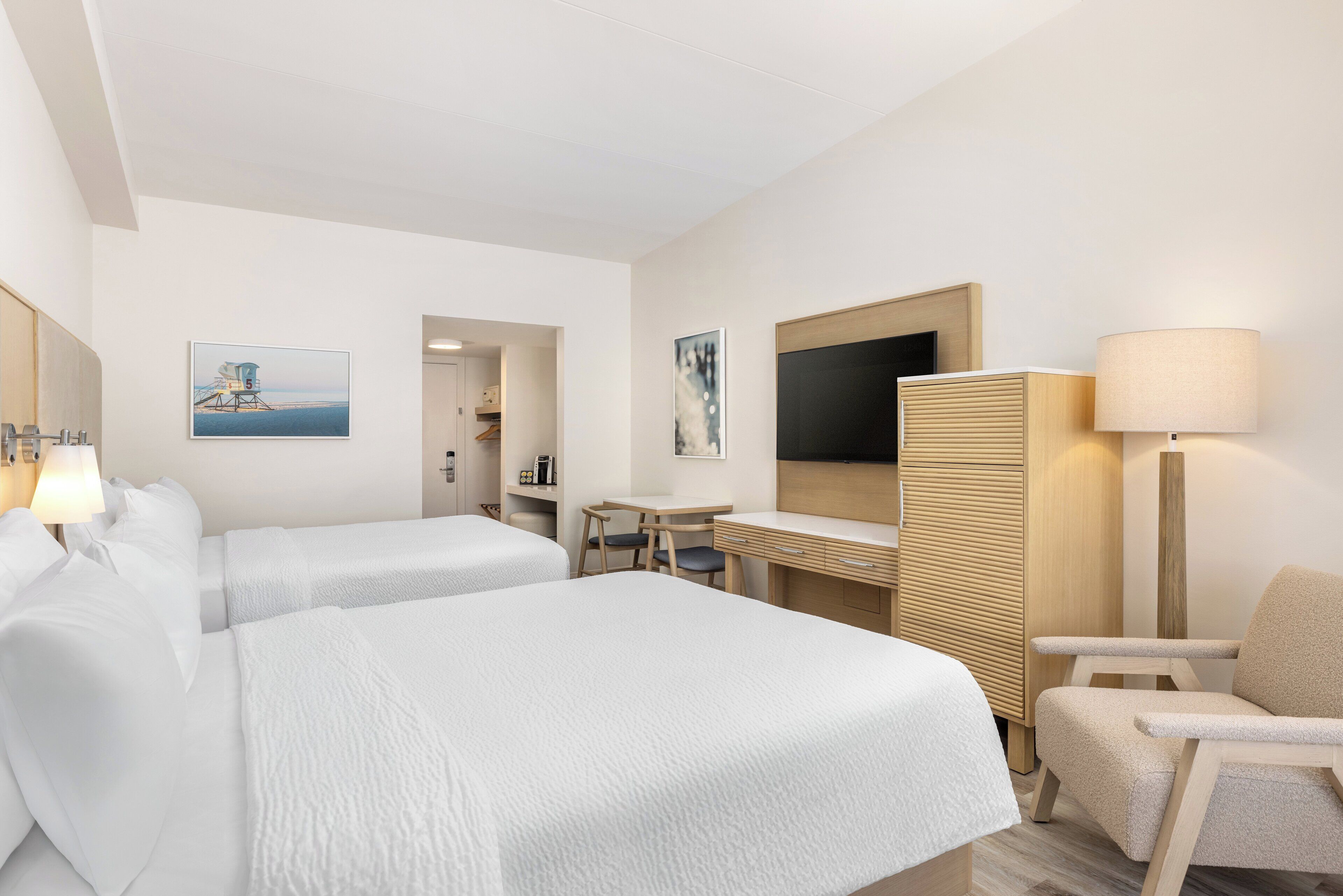 Ett hotellrum med två sängar, ett skrivbord, en stol, en TV och konstverk på väggarna.
