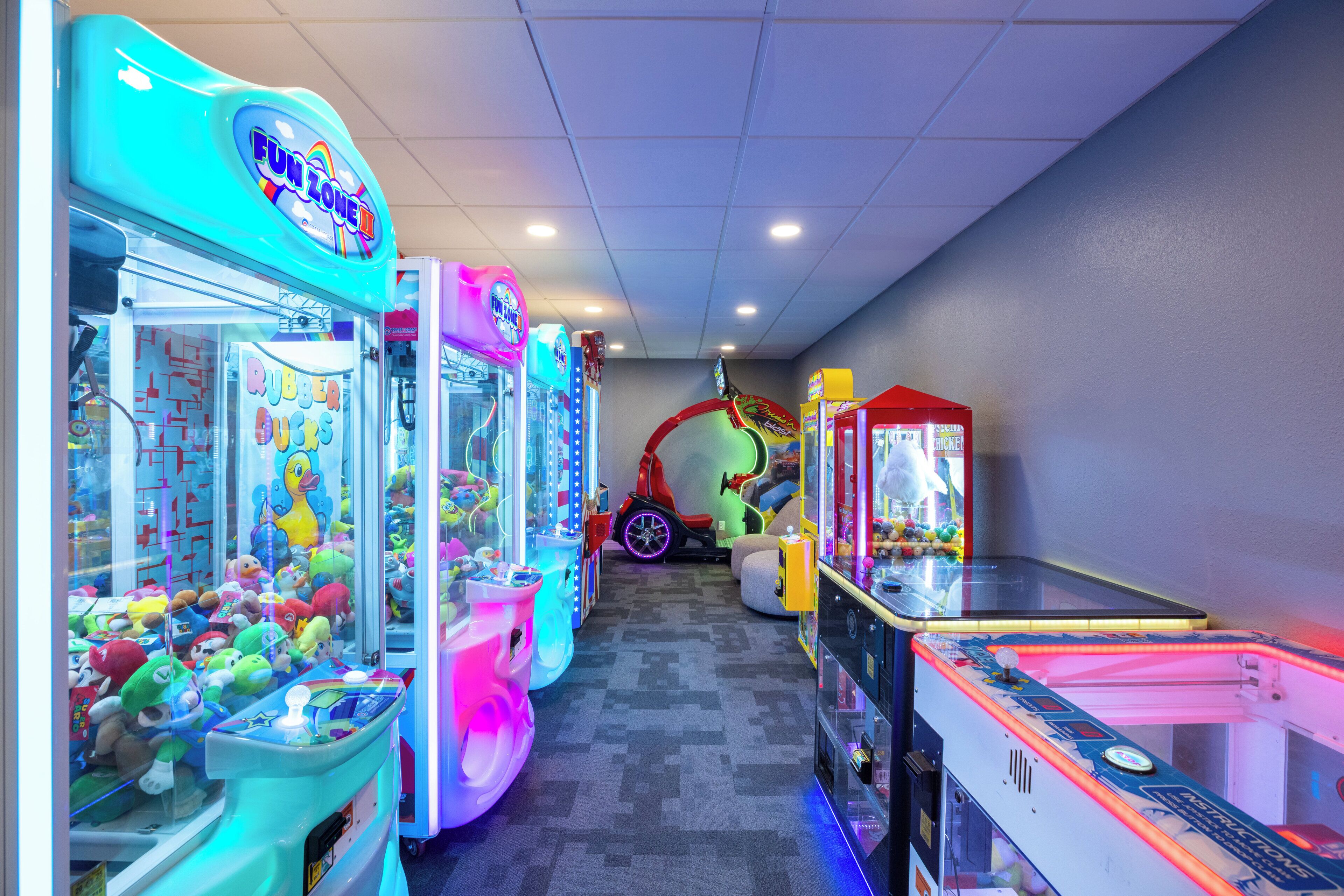 A row of brightly lit arcade machines in a room with a tiled ceiling and gray carpet.
