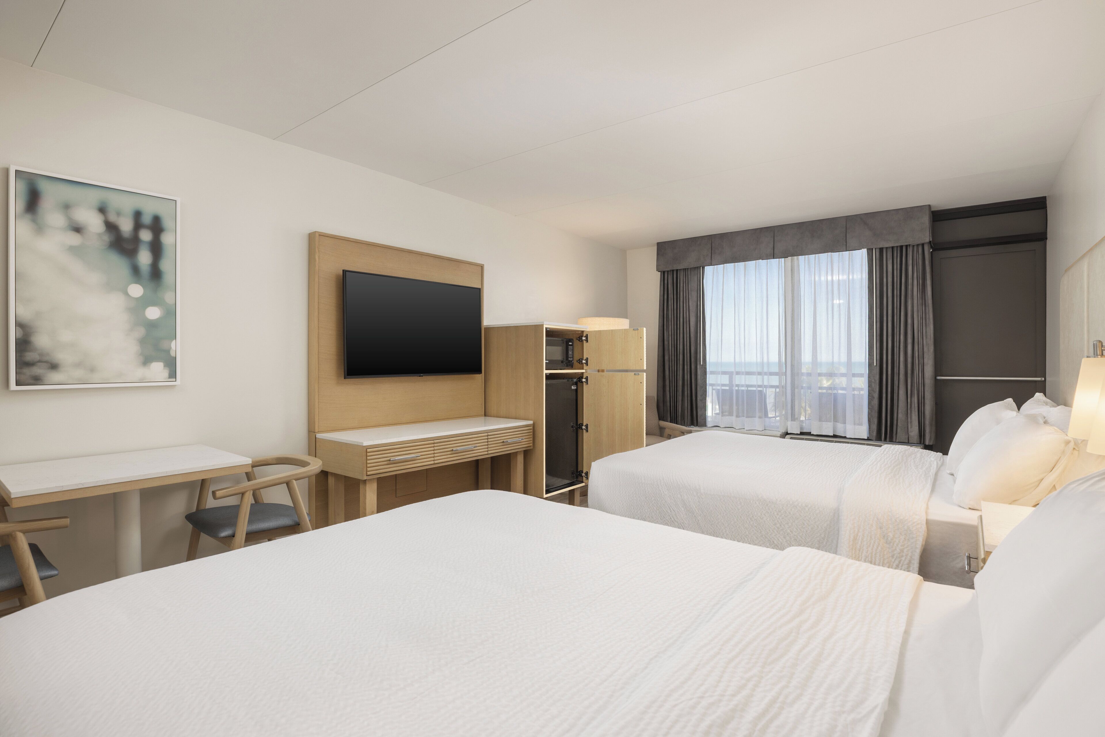A hotel room with two beds, a desk, a TV, and a window with curtains.