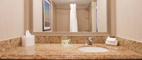 A bathroom with a granite countertop, a sink, a mirror, a towel dispenser, and a framed picture on the wall.