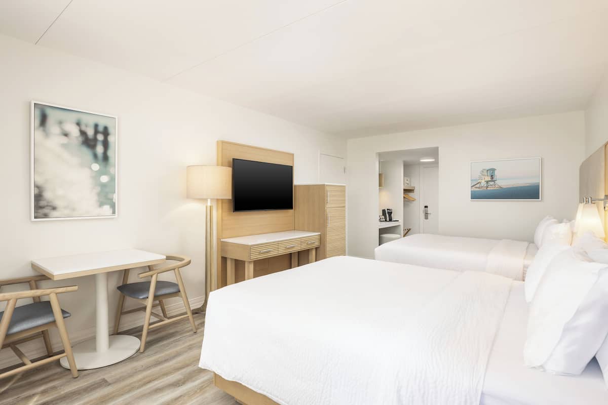 Ein Hotelzimmer mit zwei Betten, einem Schreibtisch, einem Fernseher und Bildern an den Wänden.