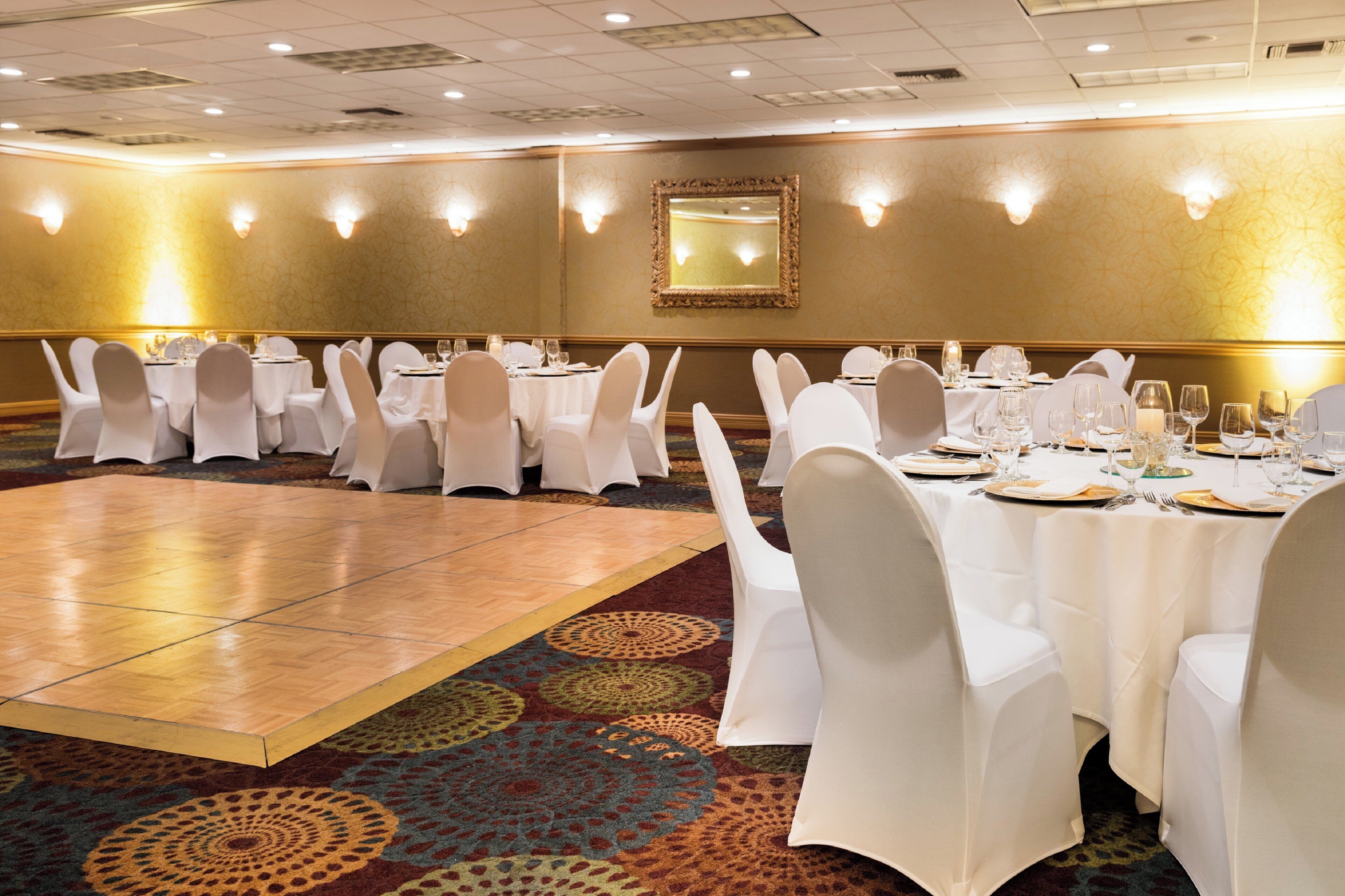 Une salle de banquet avec des tables rondes, des chaises blanches et une piste de danse.