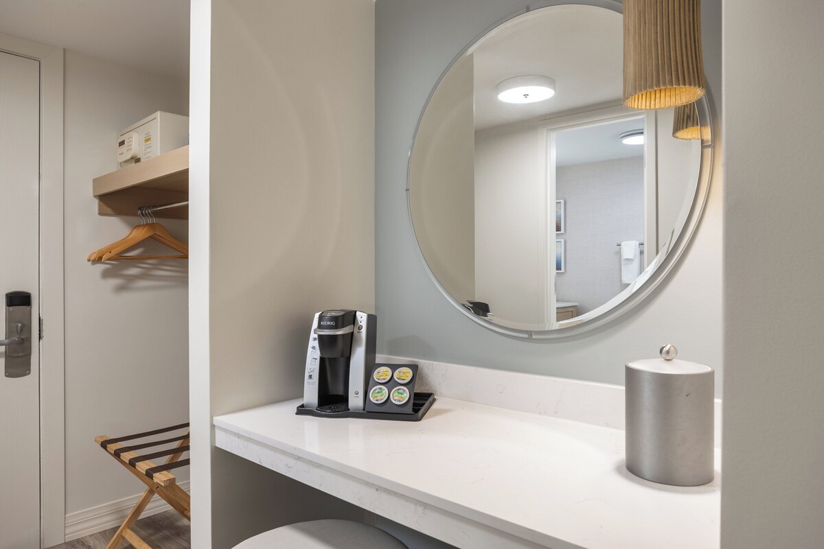 Ein modernes Badezimmer mit Kaffeemaschine, Handtuchspender und Spiegel.