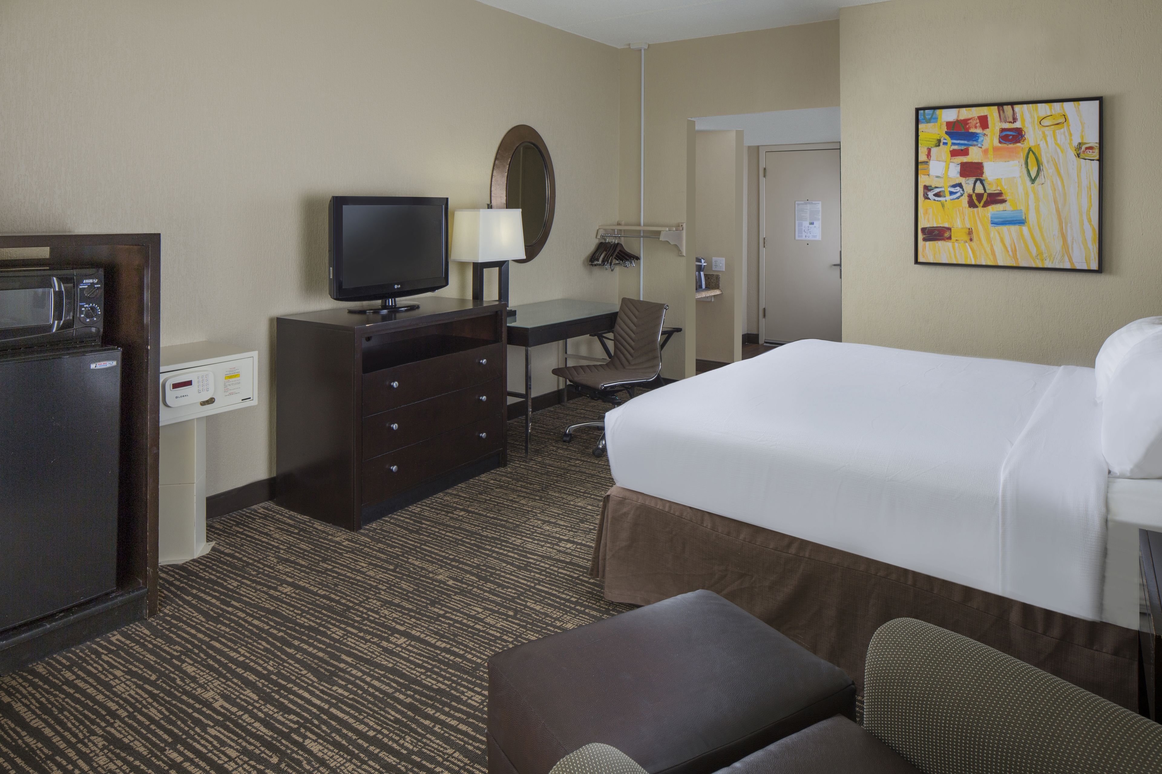 A hotel room with a bed, a desk with a chair, a television, a microwave, and a painting on the wall.