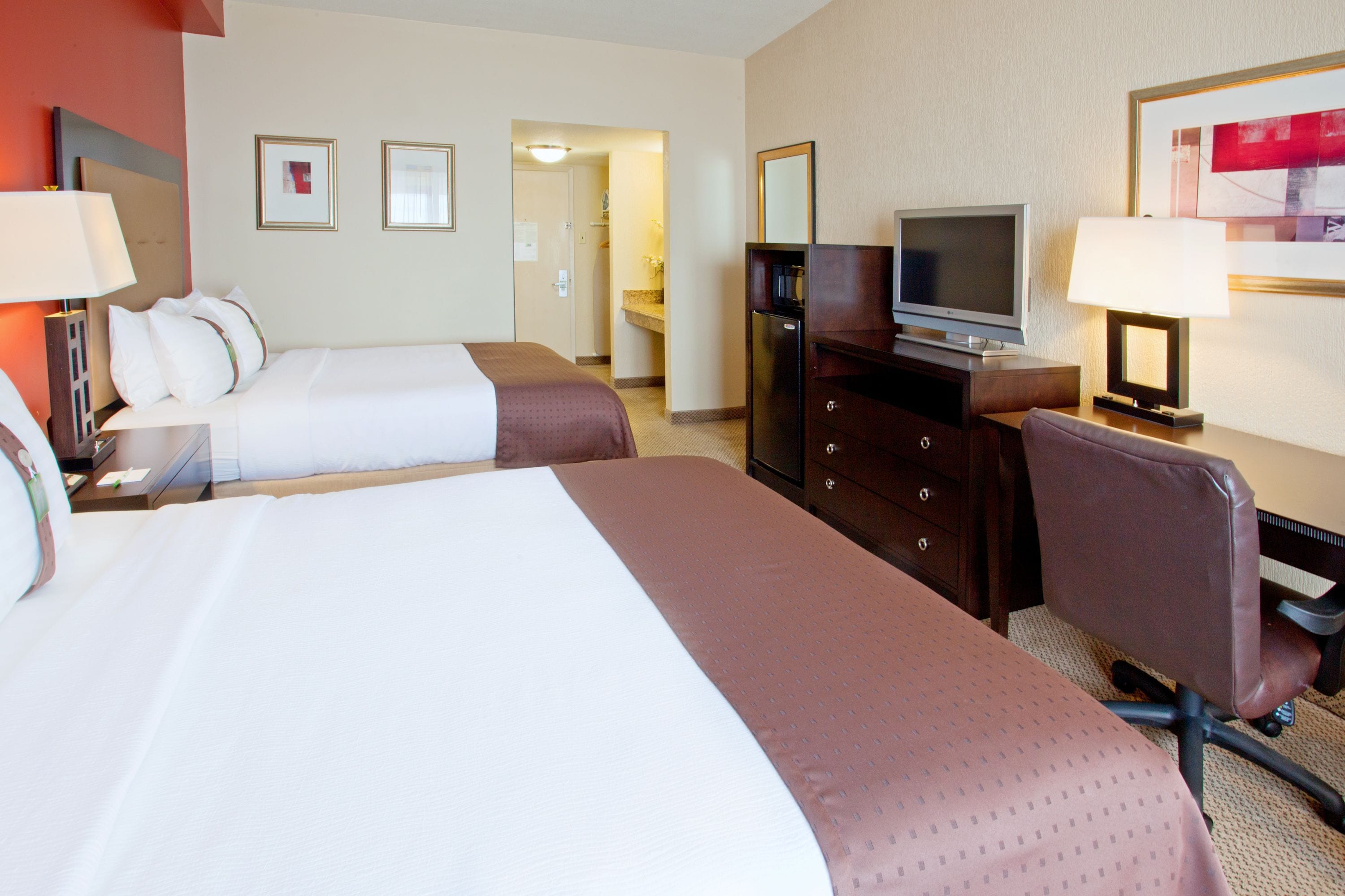 A hotel room with two beds, a TV, a desk, and a chair.