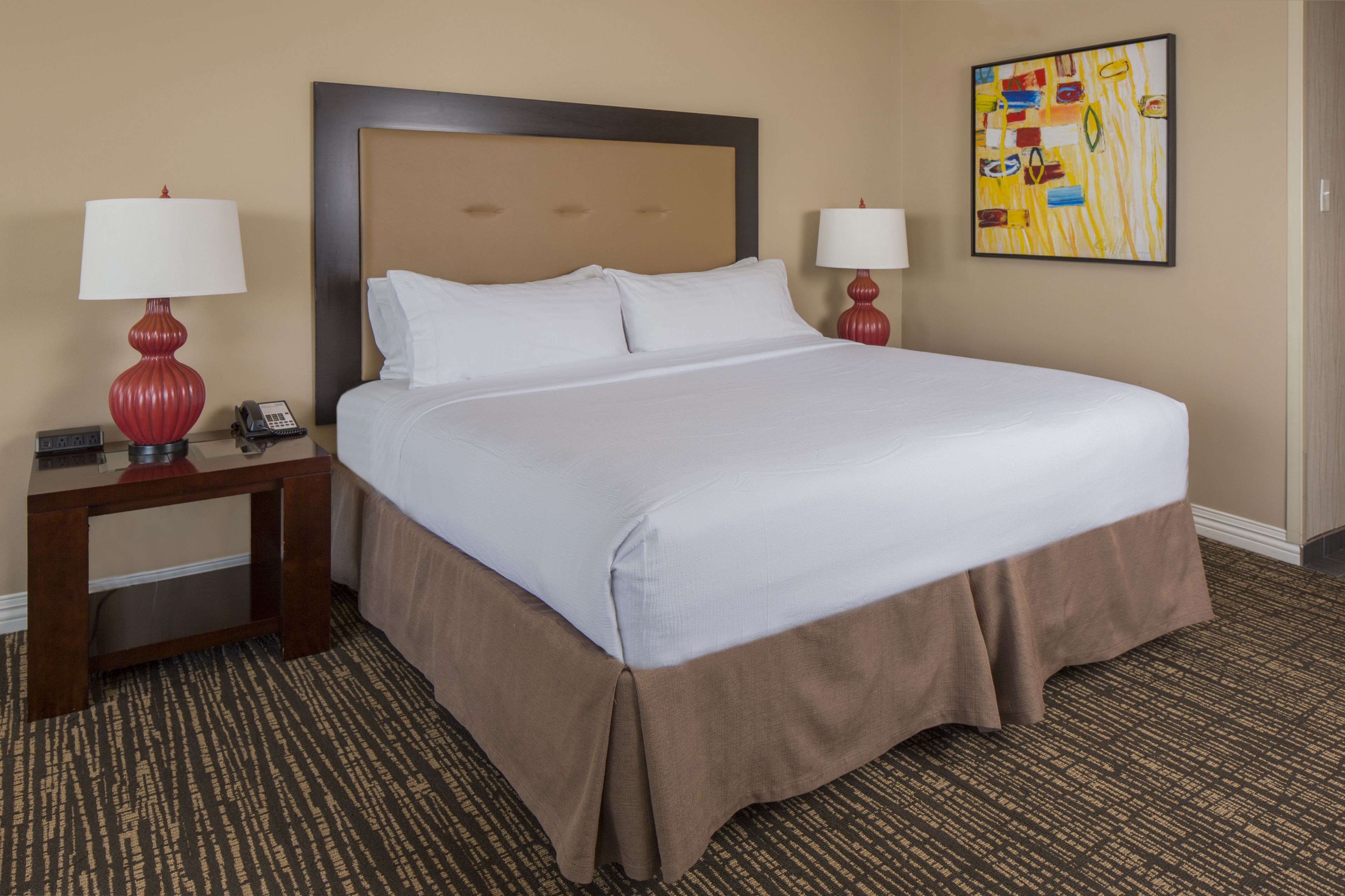 A hotel room with a large bed, two bedside tables with lamps, a telephone, and a painting on the wall.