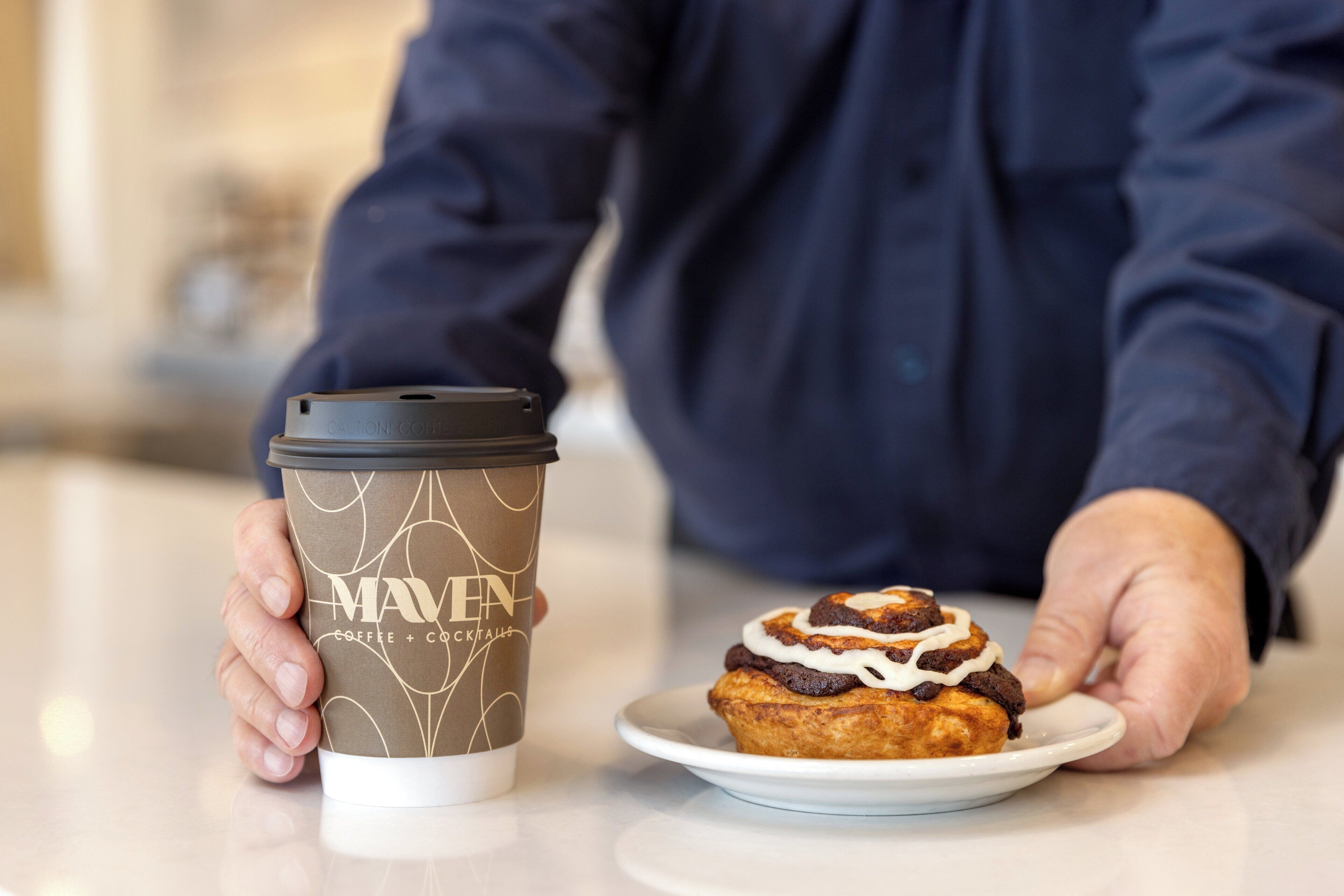 A person holding a coffee cup and a plate with a pastry.