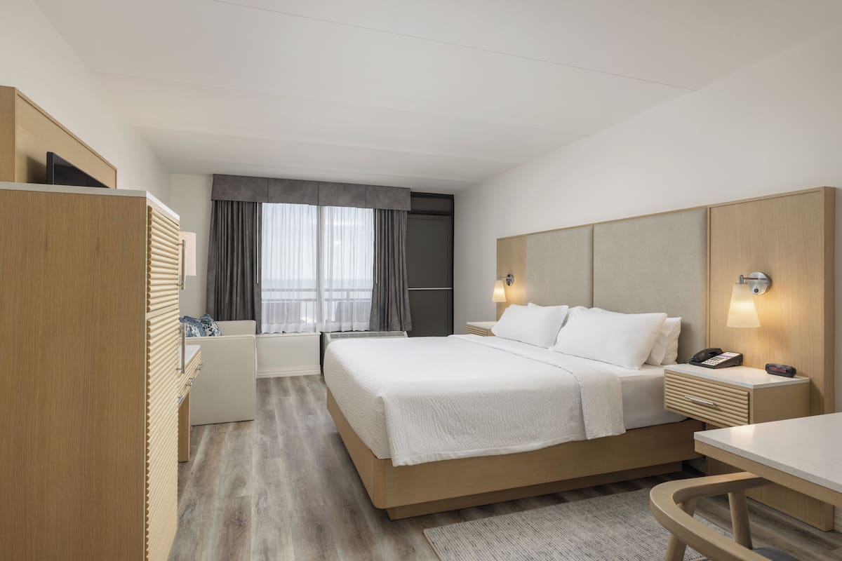 Ein modernes Hotelzimmer mit einem großen Bett, Nachttischen, einem Schreibtisch und einer Sitzecke.