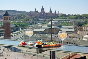 Mesa de vidrio con sushi y dos vasos de agua, con vistas a un paisaje urbano con edificios históricos.