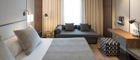 Una habitación de hotel moderna con una cama grande, un sofá, una mesita y un escritorio.