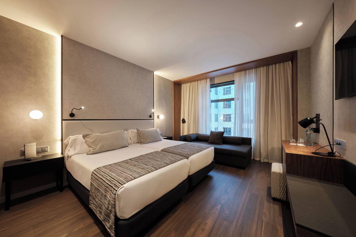 Une chambre d’hôtel moderne, dotée d’un grand lit, d’un canapé, d’un bureau et d’une fenêtre avec des rideaux.