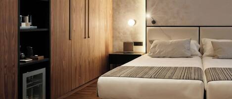 Habitación de hotel moderna con armario de madera, cama con dos almohadas, mesita de noche con lámpara y televisión integrada.