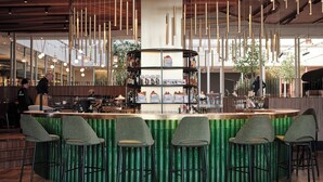 Un espace bar moderne avec un comptoir vert, de nombreux luminaires suspendus et des tabourets de bar.