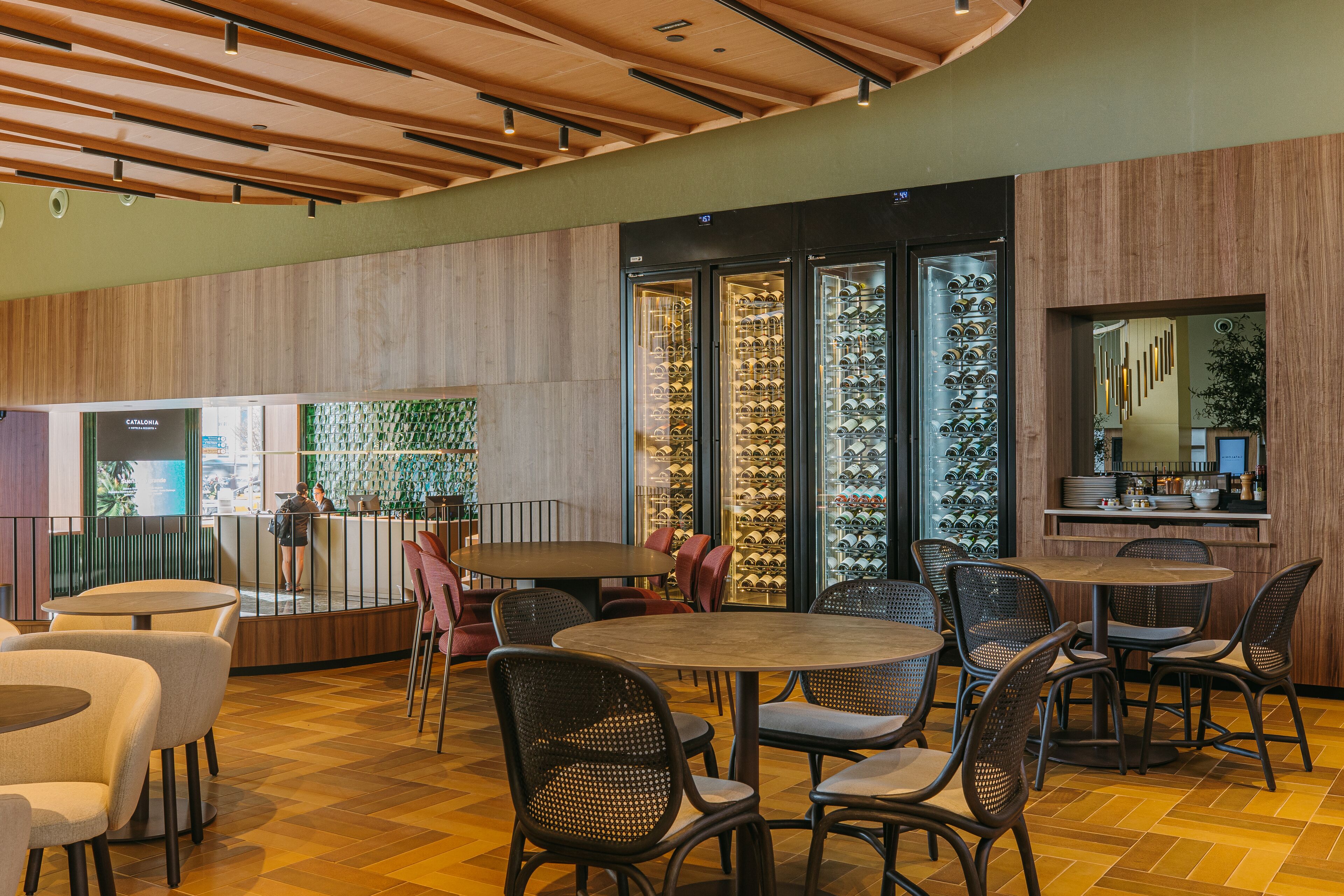 A modern interior with round tables and chairs, a wine display, and a reception area.