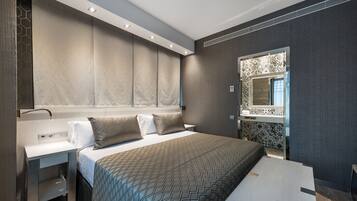 Una habitación de hotel moderna con una cama grande, una mesita de noche, un banco integrado y un espejo amplio.