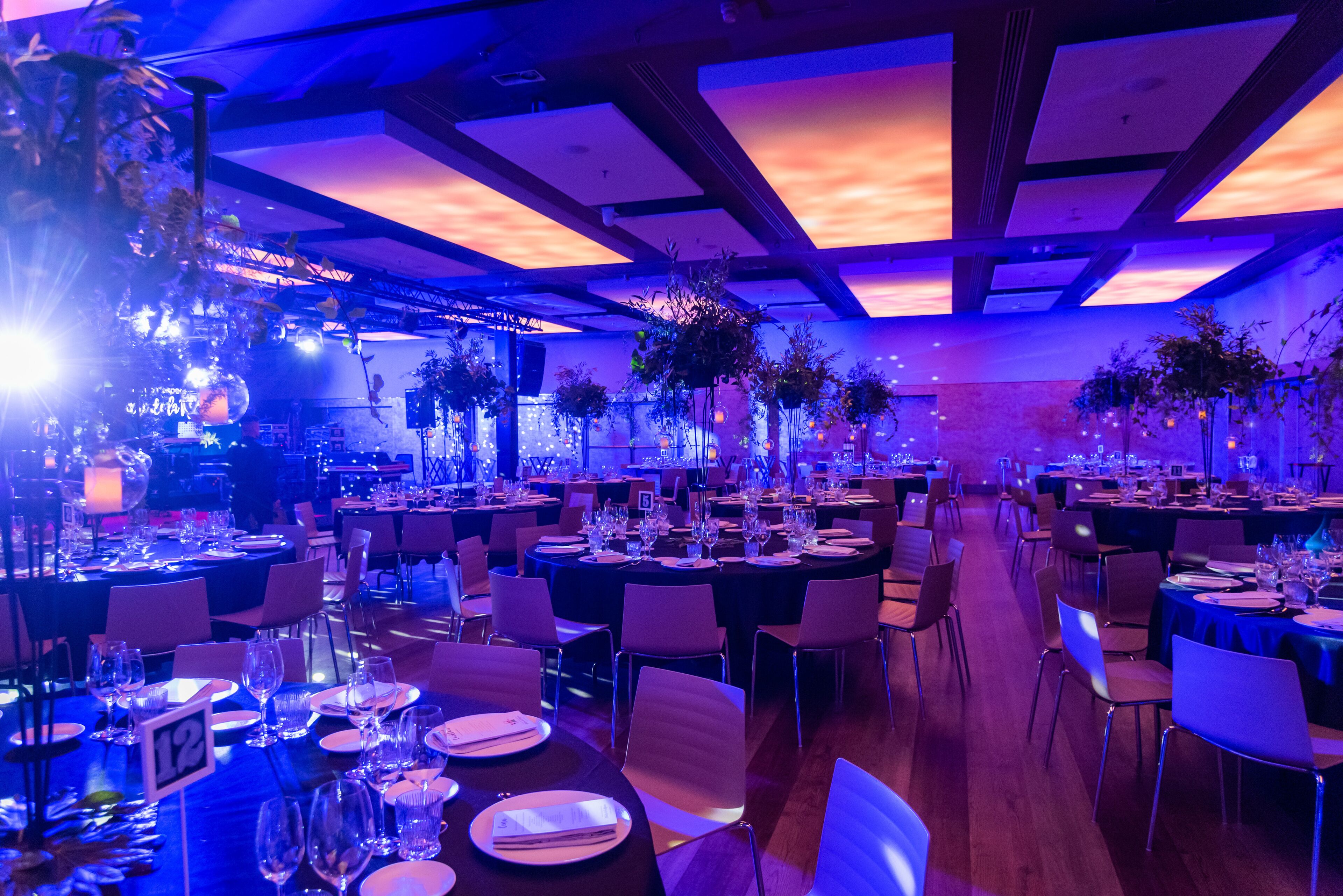 Un salón de banquetes con mesas dispuestas para un evento formal, con techo alto e iluminación moderna.