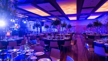 Un salón de banquetes con mesas dispuestas para un evento formal, con techo alto e iluminación moderna.
