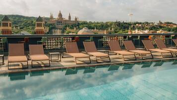 Zona junto a la piscina con sillones de descanso y vistas a edificios históricos al fondo.