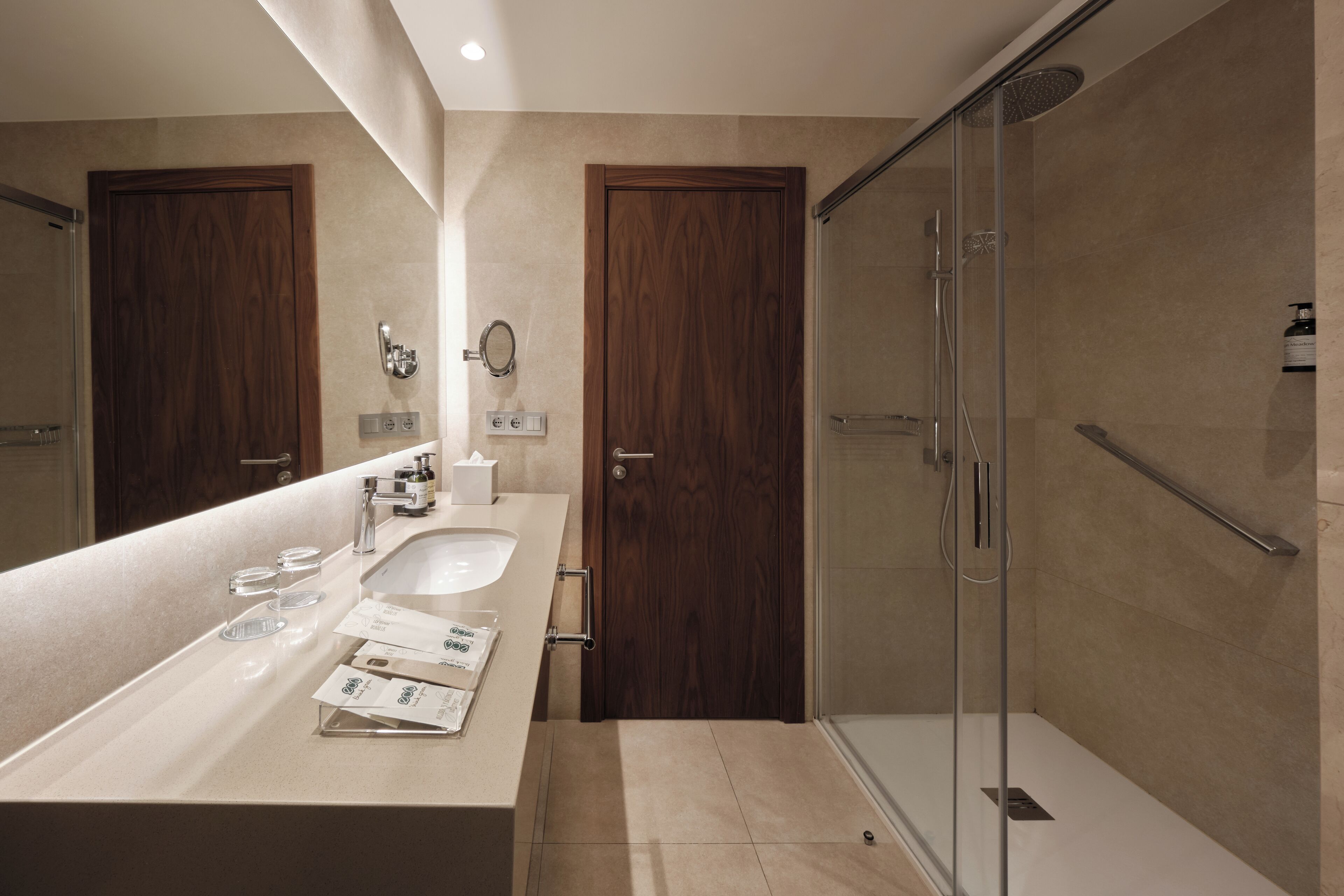 A modern bathroom with a large sink, two wooden doors, a glass shower enclosure, and a towel rack.