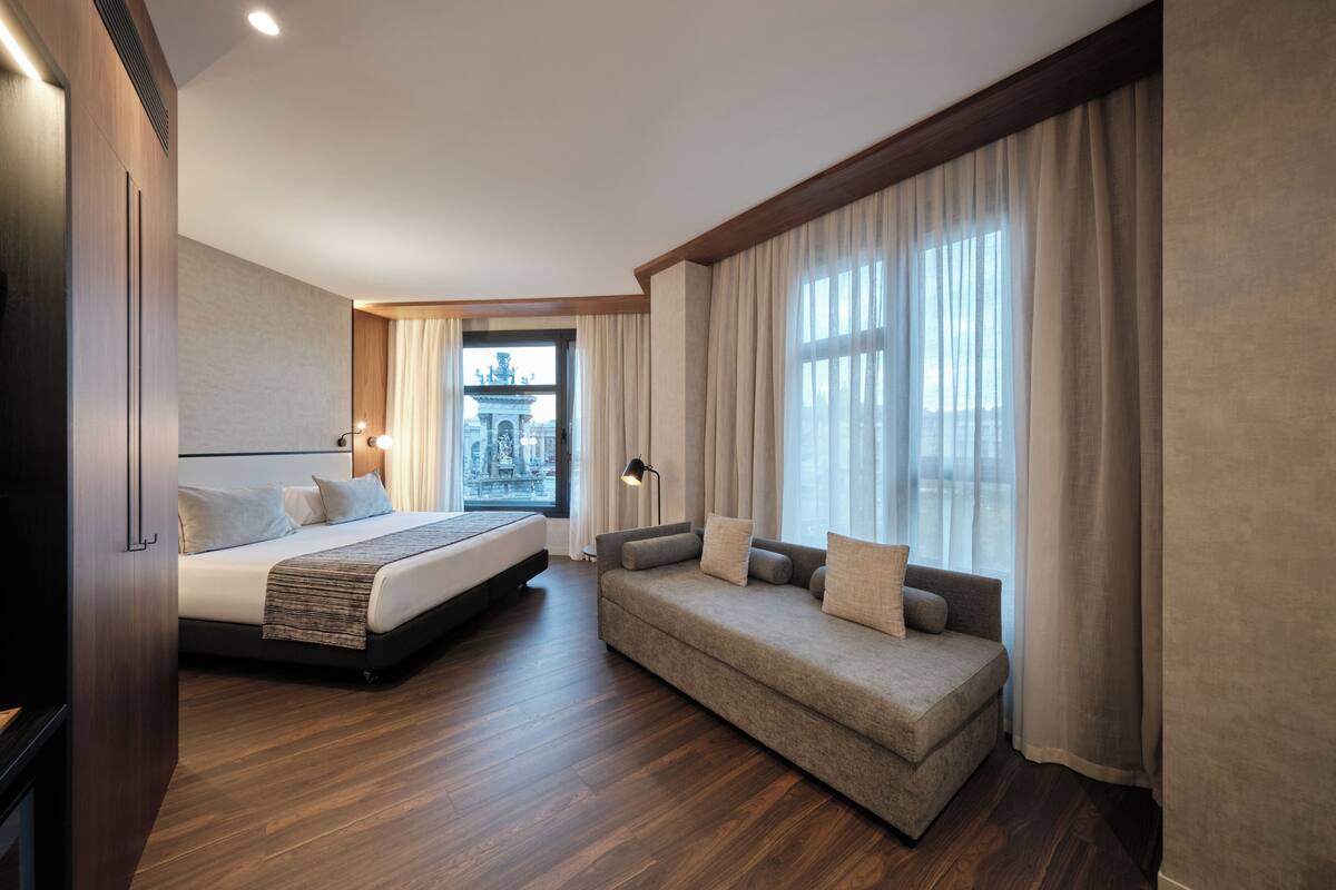 Une chambre d’hôtel moderne dotée d’un grand lit, d’un canapé, d’un parquet et offrant une vue sur le paysage urbain par la fenêtre.