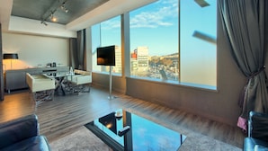 Een moderne hotelkamer met een groot raam, een flatscreen televisie, een zithoek en een bank.