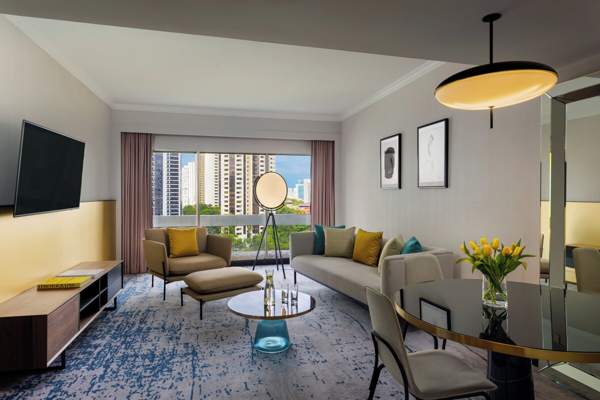 Une chambre d’hôtel moderne dotée d’une grande fenêtre, d’un téléviseur à écran plat, d’un canapé, d’une table basse et d’un coin repas.