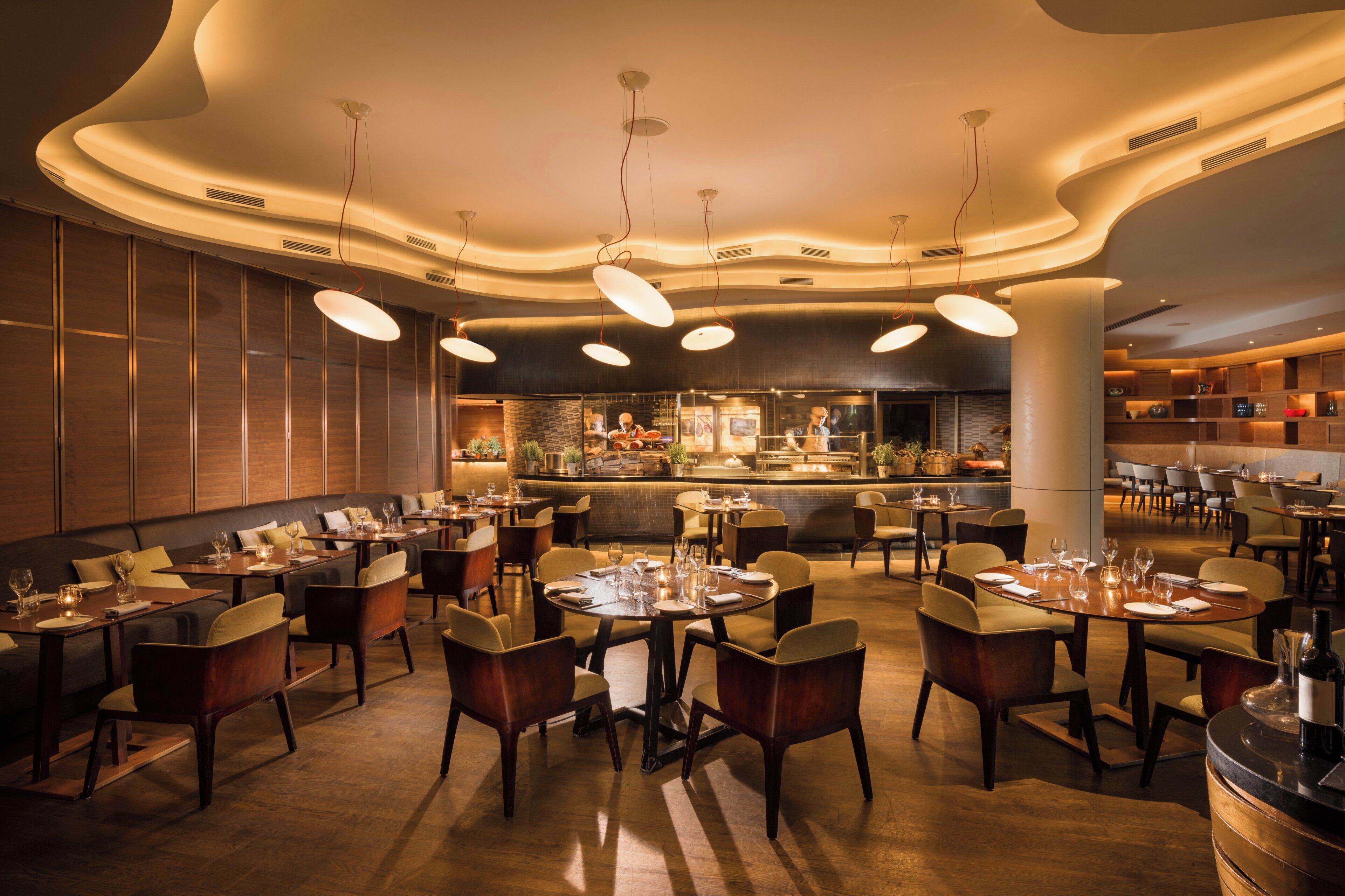 Ein modernes Restaurantambiente mit runden Tischen, Stühlen und einer Bar in der Mitte.