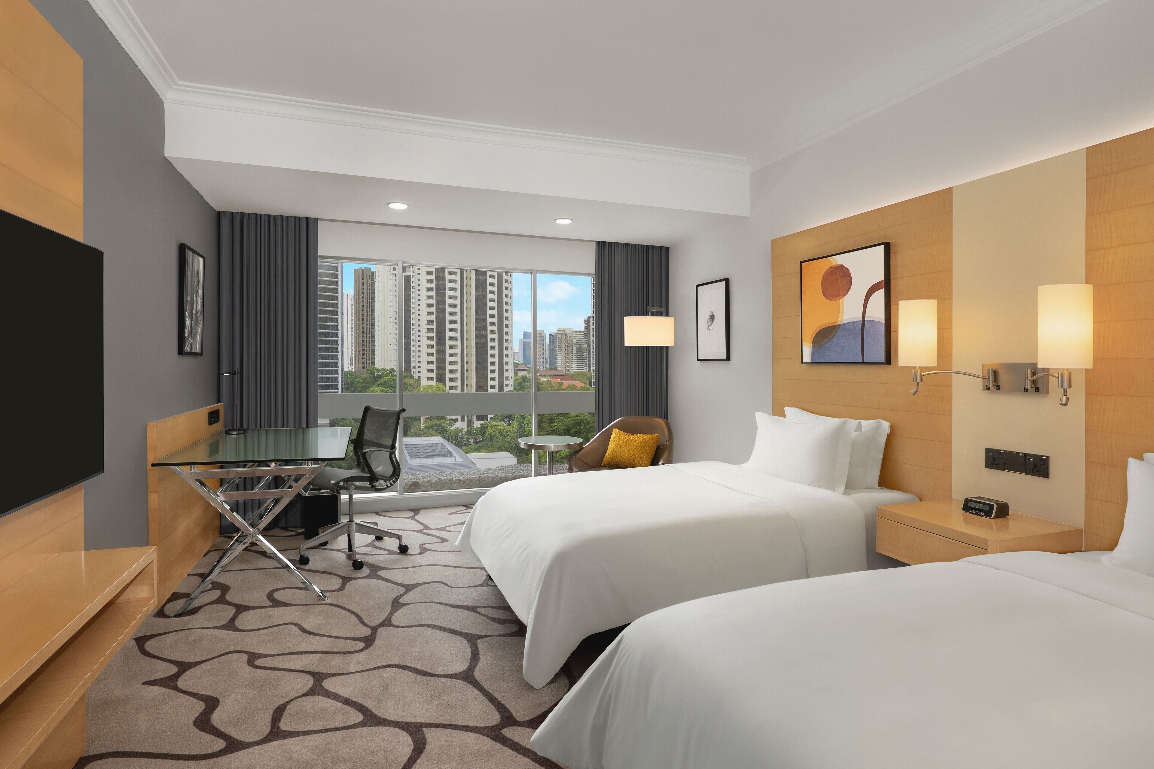 Habitación de hotel con dos camas, un escritorio, una silla, un televisor y vistas a edificios altos.