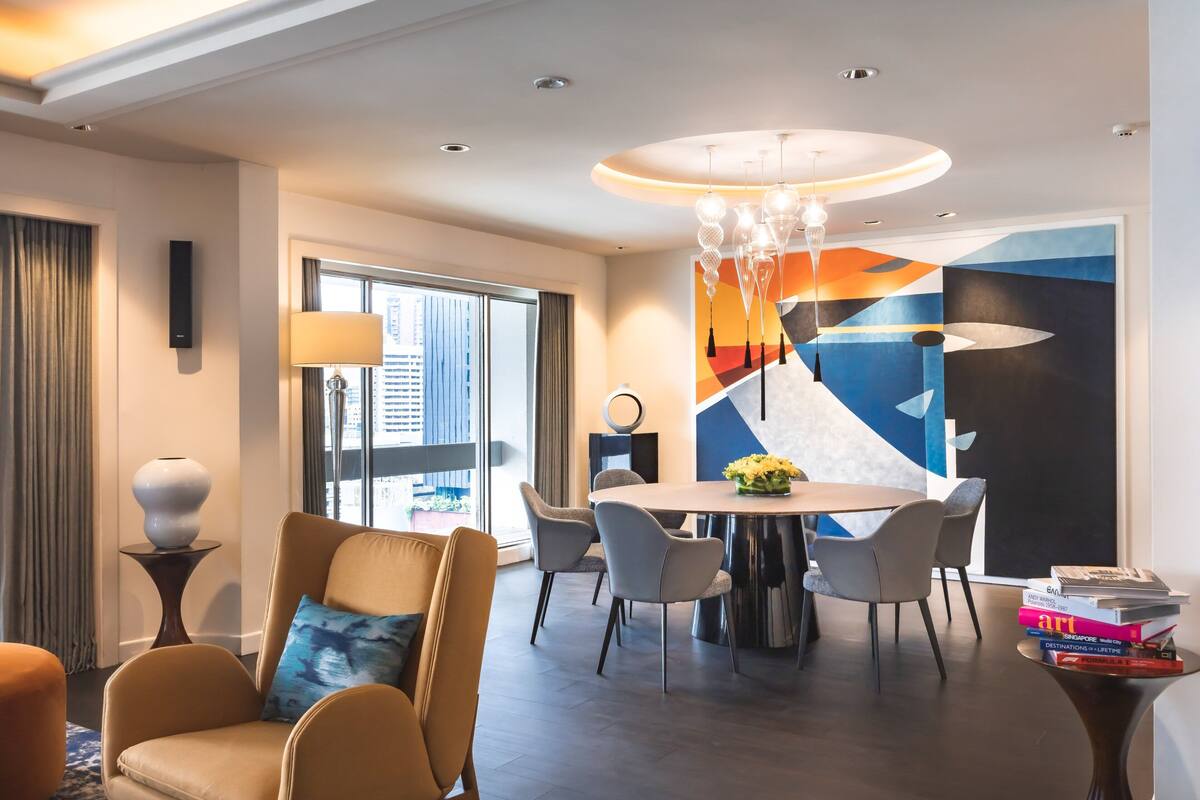 Una habitación de hotel moderna con comedor, un ventanal con vista a la ciudad y una lámpara de araña contemporánea.