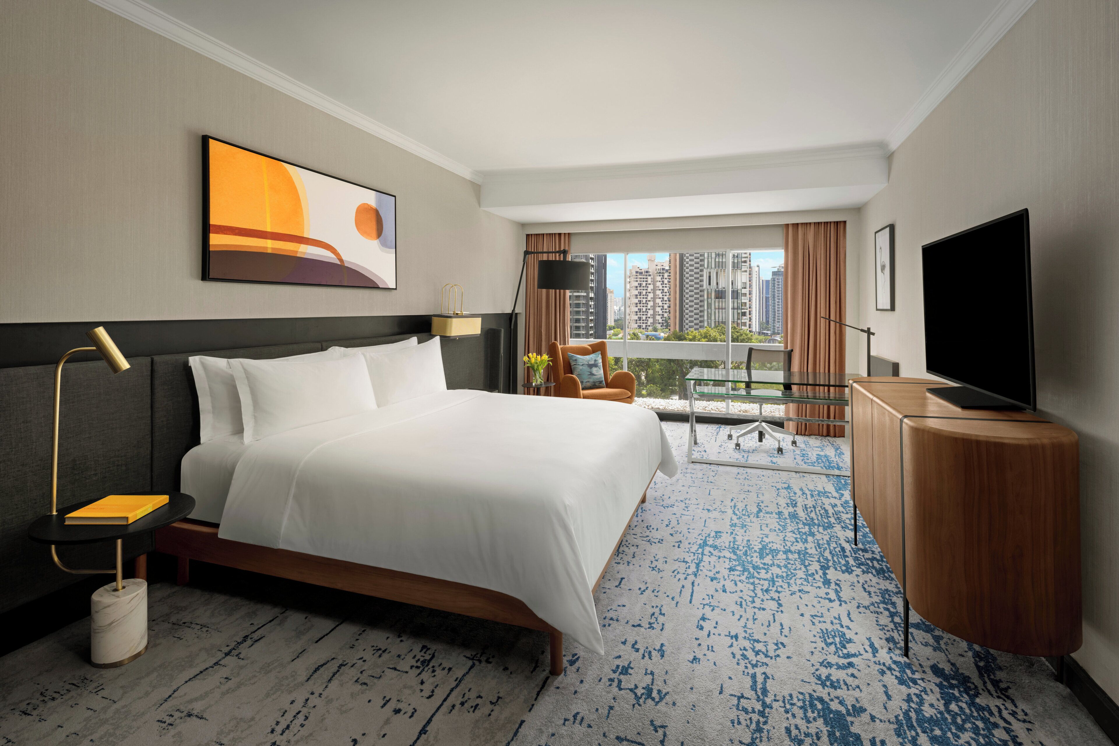 Habitación de hotel con una cama grande, un escritorio, un televisor y vistas a la ciudad.