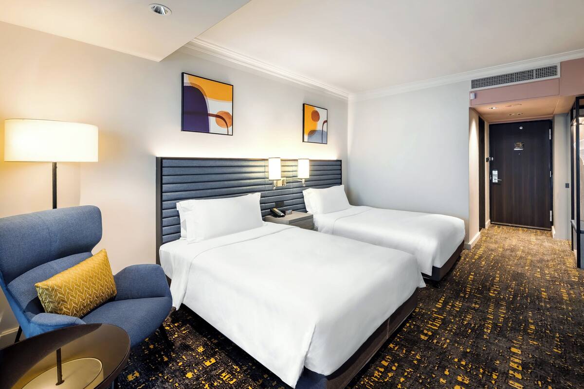 Habitación de hotel con dos camas, un sofá, una lámpara y obras de arte en la pared.