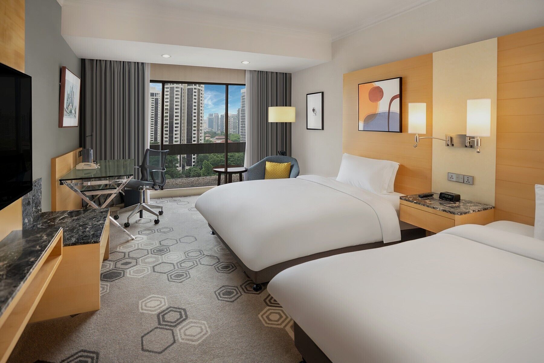 A hotel room with two beds, a desk, a chair, a TV, and a view of tall buildings.