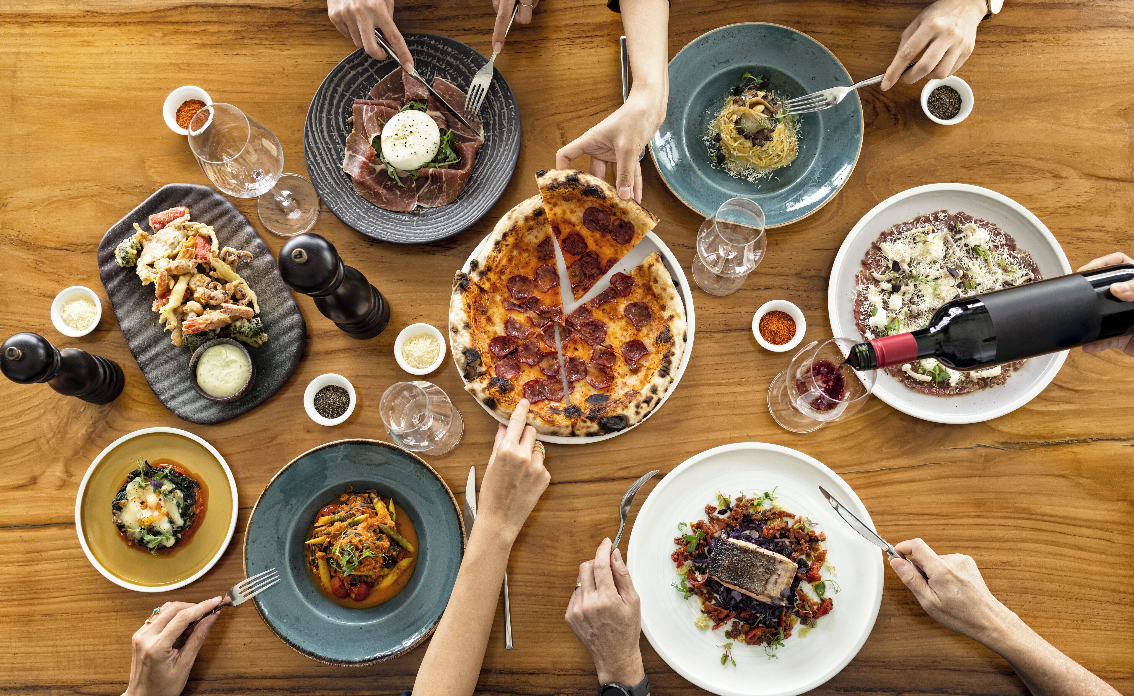 A group of people dining around a wooden table with various dishes.