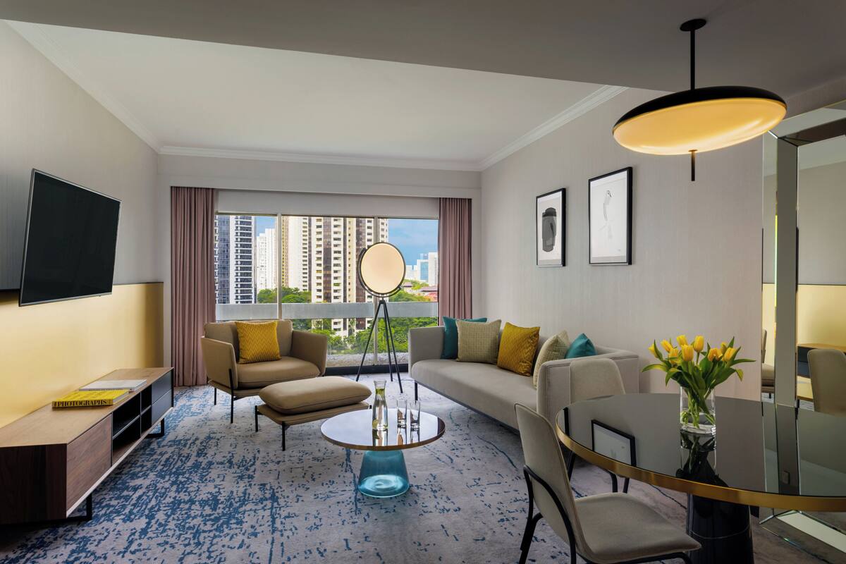 Una habitación de hotel moderna con un ventanal grande, un televisor de pantalla plana, un sofá, una mesa de centro y un área de comedor.